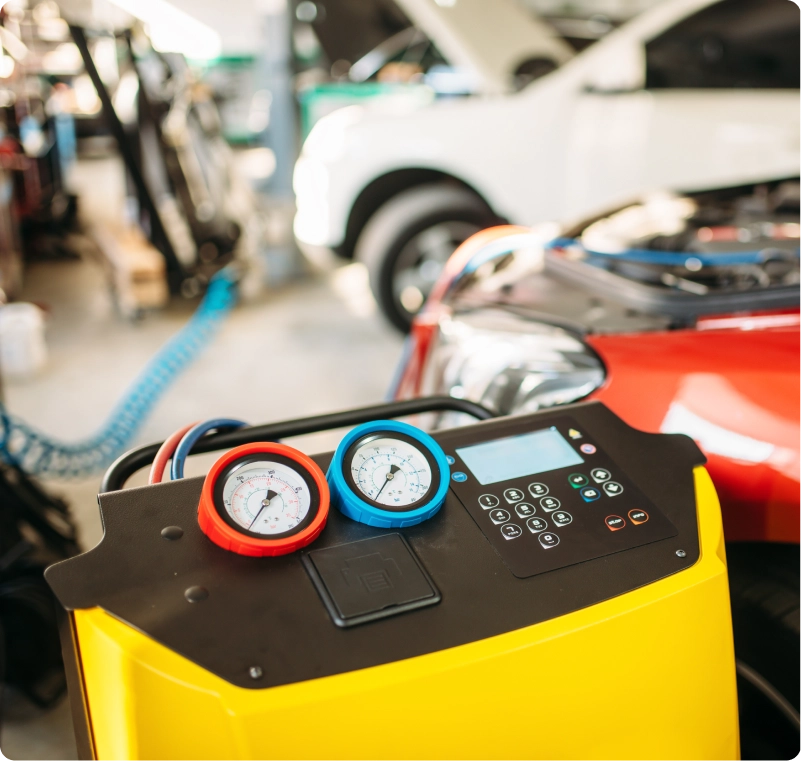 Automotive AC service machine with pressure gauges beside a car in a repair shop