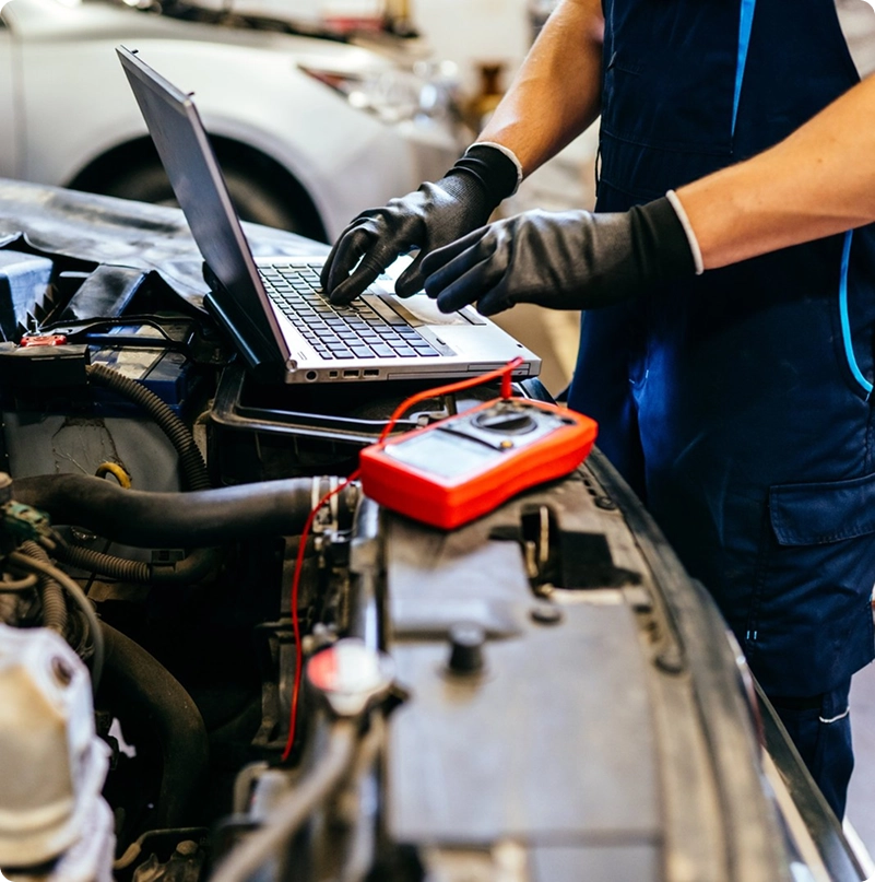 Mechanic using a laptop and diagnostic equipment beside an open engine bay
