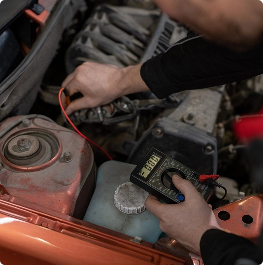 Mechanic testing electrical components in a car engine bay with a handheld diagnostic device