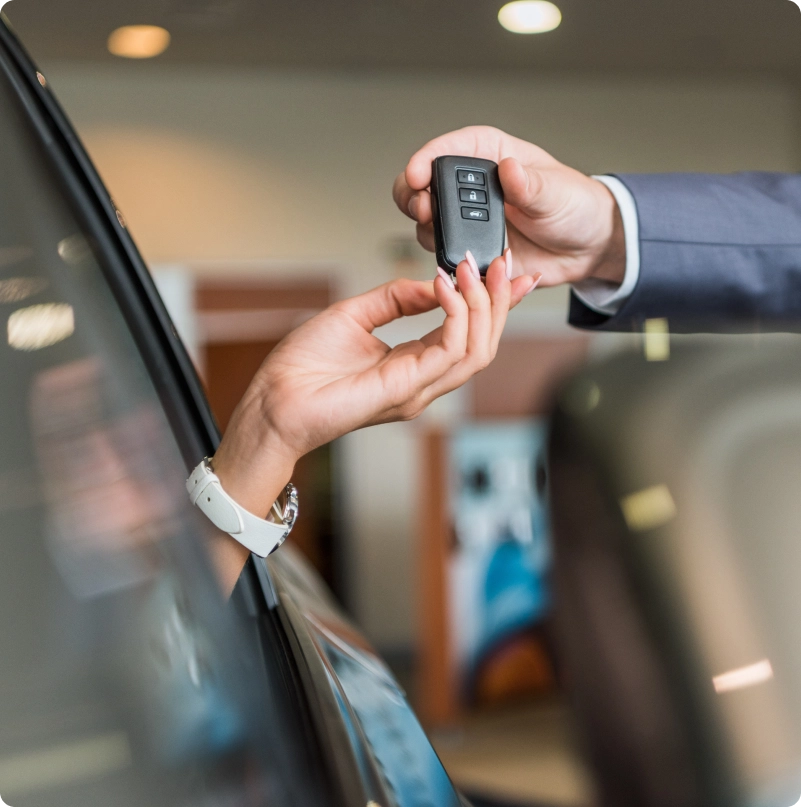 Person handing a car key to a buyer beside a vehicle